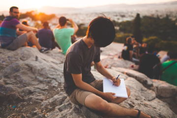 Un ragazzo scrive su una montagna circondato da altre persone