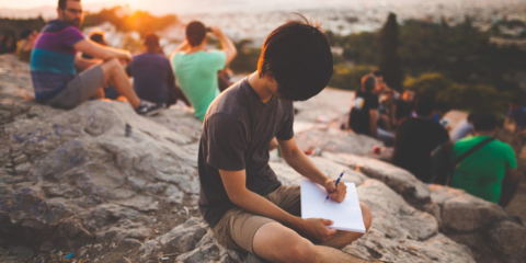 Un ragazzo scrive su una montagna circondato da altre persone