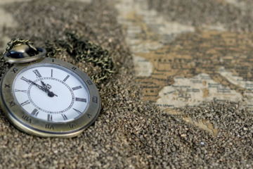Un orologio da taschino sulla sabbia e una cartina antica